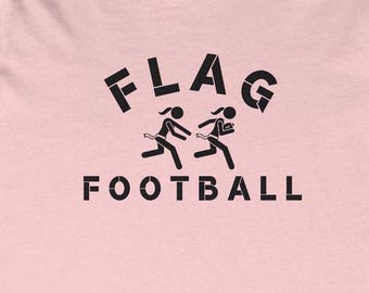 May include: Pink t-shirt with black text that reads "FLAG FOOTBALL" and a graphic of two stick figures playing flag football.