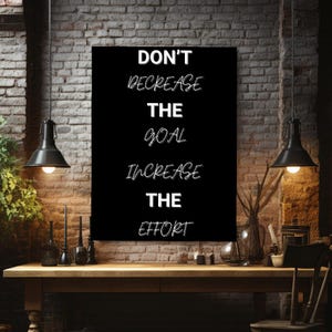 May include: A rectangular black wall art piece featuring white text that reads: DON'T DECREASE THE GOAL INCREASE THE EFFORT. The lettering uses a mix of bold sans-serif and stylised script fonts, creating a high-contrast motivational display.