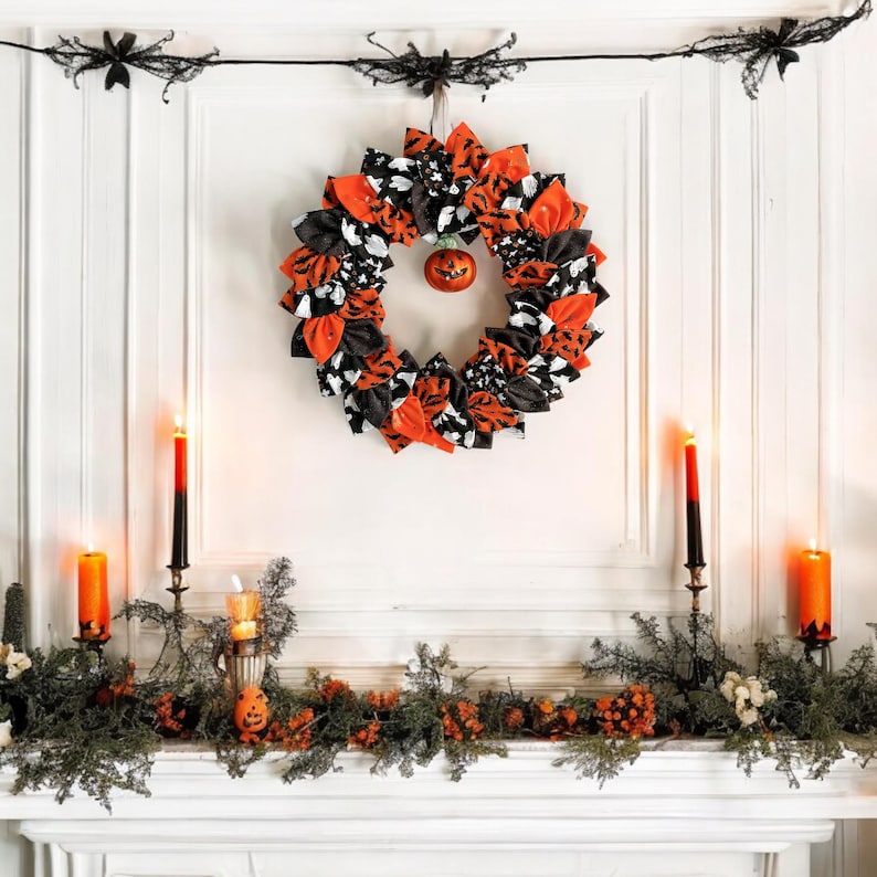 May include: A black, white, and orange Halloween wreath with a small pumpkin ornament hanging in the center. The wreath is decorated with black and white fabric bows and orange fabric. The wreath is hanging on a white wall above a fireplace mantel decorated with greenery and candles.