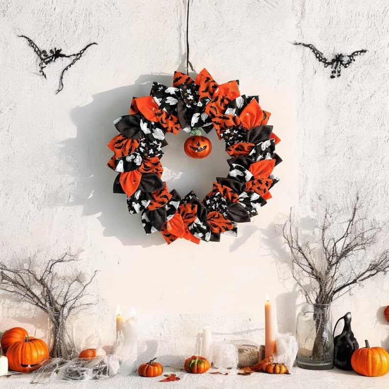 May include: A Halloween wreath made of fabric scraps in orange, black, and white. The wreath is decorated with a small orange jack-o'-lantern and black bats.