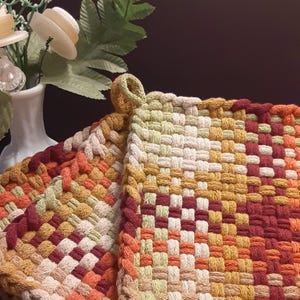 May include: Two woven pot holders in a red, white, yellow, and green color scheme. The pot holders are made of a thick, textured yarn and have a square shape.