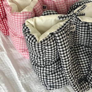 May include: Close-up of three pet beds in red, pink, and black and white gingham patterns. The beds have a soft, quilted appearance with cream-colored interiors. The text "MADE BY HAUSIE" is visible on the side of the beds.