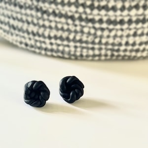 Peut inclure: Une paire de boucles d'oreilles clous en nœuds noirs. Les boucles d'oreilles sont en pâte polymère et ont un design simple et moderne.