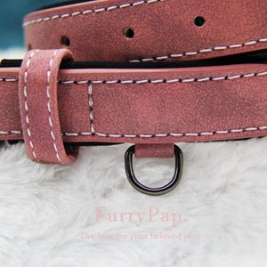 May include: A pink leather dog collar with white stitching and a silver D-ring. The collar is made of a soft, textured material.