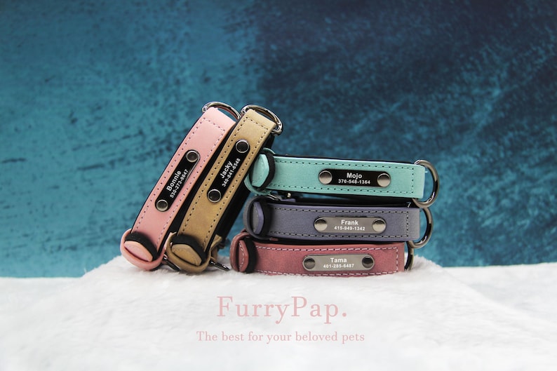 May include: Four personalised leather dog collars stacked on top of each other. The collars are in shades of pink, blue, grey, and light blue. Each collar has a silver name tag with a name and phone number.