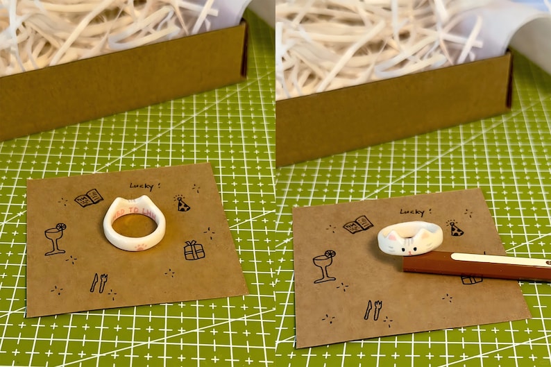 K&ouml;nnte beinhalten: Zwei wei&szlig;e Keramikringe mit unterschiedlichen Designs. Ein Ring tr&auml;gt die Aufschrift "WED TO EAT". Der andere Ring zeigt ein Katzen Gesicht mit rosa Ohren und einer rosa Nase. Beide Ringe liegen auf braunem Papier mit schwarzen Zeichnungen von Partyartikeln.