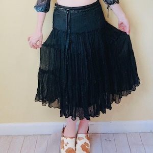 May include: A black tiered skirt paired with a patterned, cropped top. The top features a V-neck and three-quarter sleeves. The outfit is completed with cow-print slip-on shoes.