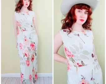 May include: A sleeveless, floor-length dress with a floral pattern featuring pink roses and green leaves. The dress is paired with a light gray hat. The dress has a scoop neckline and a fitted waist. The background is a light yellow color.