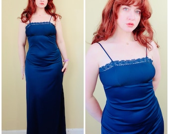 May include: A floor-length dark blue gown featuring a ribbed bodice with a delicate lace trim along the straight neckline. The garment has thin spaghetti straps and a smooth, flowing skirt that extends to the floor, creating a sleek silhouette.