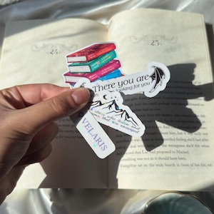 May include: A collection of three die-cut stickers featuring a stack of colorful books, a mountain range with the text "stars who listen and dreams that are answered," and a banner with the text "There you are" and "VELARIS" with holographic accents.