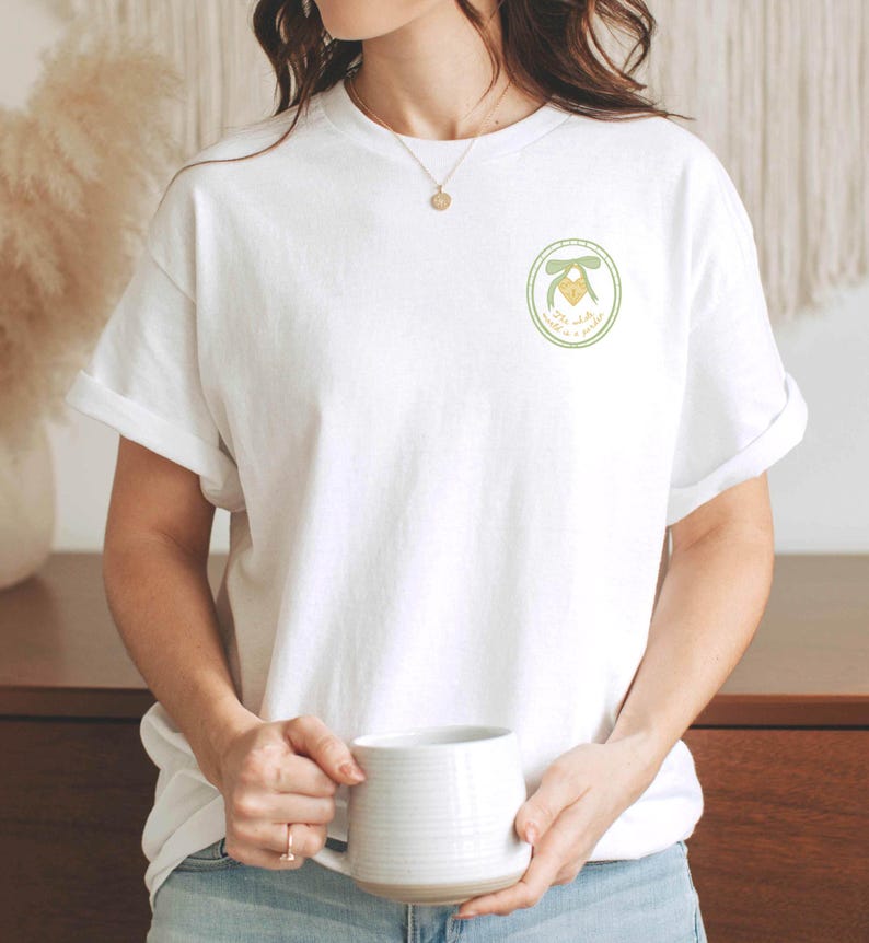 May include: A white t-shirt with a green circle design featuring a yellow heart with a green bow and the text "You're my happy place".