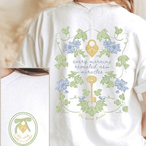 May include: White t-shirt with a floral design and the text "every morning revealed new miracles" and "The Secret Garden".