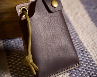 May include: A brown leather wallet with a gold button and a green cord. The wallet is on a striped fabric background.