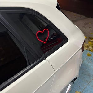 May include: A white car with a red heart sticker on the back window.