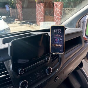 May include: A black plastic smartphone mount attached to the dashboard of a vehicle, holding a smartphone with a screen displaying the time 14:36 and a logo with the text 3D BayDesign Oto Aksesuar positioned next to a vehicle infotainment screen.