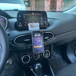 May include: A black smartphone mounted on a car air vent, displaying a logo with the text 3D BayDesign. Above the phone, a small white rectangular sign is attached to the infotainment screen, also featuring the 3D BayDesign logo and text.