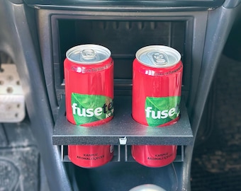 May include: Two red cans of Fusetea Watermelon Flavored Iced Tea in a black car cup holder. The text on the cans reads "Fusetea Ice Tea" and "Karpuz Aromali Icecek".