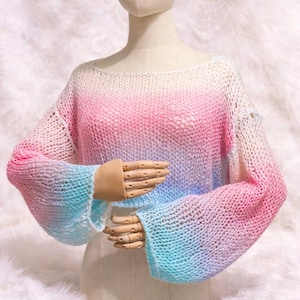 Può includere: Un maglione lavorato a maglia con una sfumatura di colore dal bianco al rosa e al blu. Il maglione ha maniche lunghe e ampie e una trama larga e aperta. L'indumento è esposto su un manichino.