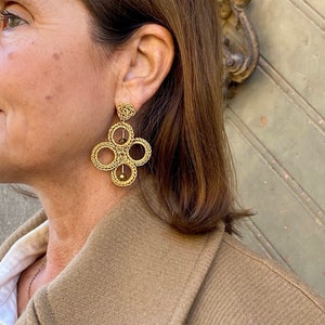 May include: Gold tone earrings with a geometric design featuring four interlocking circles. The earrings have a small gold bead at the bottom.