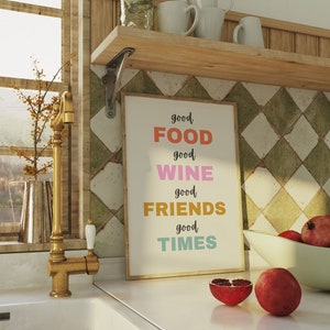 Peut inclure: Intérieur d'une cuisine avec un plan de travail blanc, un robinet doré et un évier blanc. Un imprimé encadré avec le texte "good FOOD good WINE good FRIENDS good TIMES" est accroché au mur. Un bol de grenades rouges est sur le comptoir.