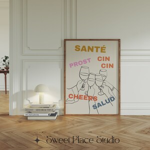 May include: A beige poster with a black line drawing of five hands holding up wine glasses. The words "Sant&eacute;", "Prost", "Cin Cin", "Cheers", and "Salud" are written in different colours around the glasses.