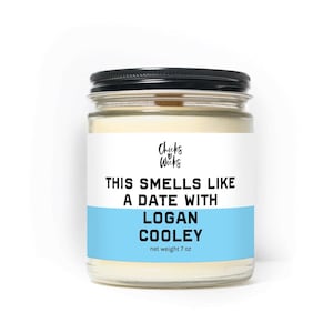 May include: A glass jar candle with a black lid and a white label. The label reads "THIS SMELLS LIKE A DATE WITH LOGAN COOLEY" over a light blue band. The candle's net weight is 198 grams.