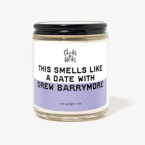 Pode incluir: Um frasco de vidro para velas com tampa preta e um rótulo roxo. O rótulo diz "Chicks & Wicks" e "This smells like a date with Drew Barrymore". A vela pesa 7 oz.