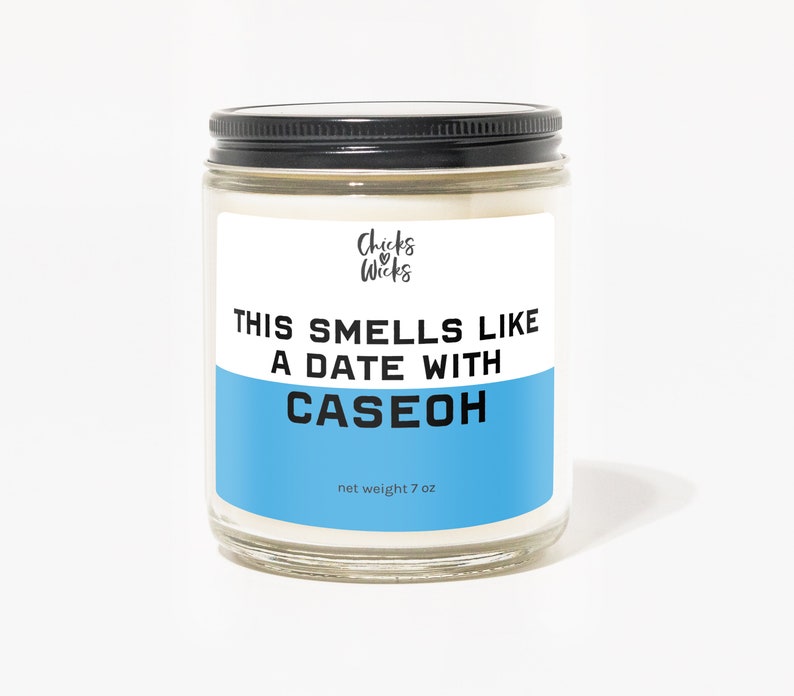 Puede incluir: Un tarro de vidrio para velas con tapa negra y una etiqueta azul que dice "This smells like a date with CASEOH". La etiqueta tambi&eacute;n incluye el texto "Chicks & Wicks" y "net weight 7 oz".