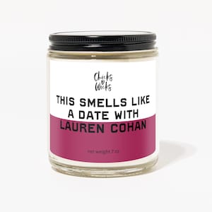 Puede incluir: Un tarro de vidrio para velas con tapa negra y una etiqueta rosa y blanca. La etiqueta dice "Chicks & Wicks" y "This smells like a date with Lauren Cohan". El tarro es de 7 oz.