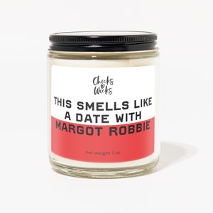 May include: A glass candle jar with a black lid and a red and white label. The label reads "This smells like a date with Margot Robbie" and "Chicks & Wicks". The candle is 7 oz.