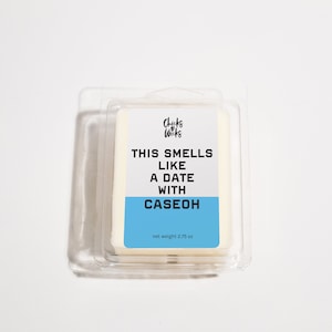 May include: A white wax melt in a clear plastic container with a blue label that reads "This smells like a date with Caseoh" and "Chicks & Wicks" in a black heart logo. The label also states "net weight 2.75 oz".