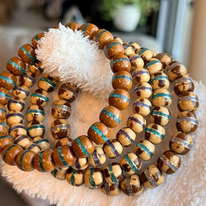 May include: A collection of four beaded bracelets featuring round wooden beads in shades of brown and tan. Each bead is accented with a central horizontal band of shimmering glitter in either turquoise or purple, creating a textured appearance.