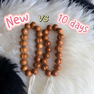 May include: Two strands of smooth, light brown wooden beads, each featuring a central horizontal groove and a white tassel at the bottom. The text New vs 10 days is displayed above the bead strands to show a comparison of their appearance.