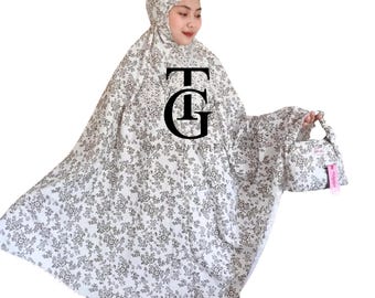 May include: White and gray floral prayer garment set. The set includes a head covering, a long, flowing robe, and a matching small handbag. The fabric is patterned with a delicate floral design. The garment has the letters "TG" printed on the front.