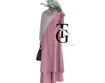 Puede incluir: Un atuendo modesto de color rosa empolvado con una camisa abotonada de manga larga y pantalones de pernera ancha a juego. El atuendo se combina con un velo de color claro y un bolso negro. La imagen incluye el texto "CHAISANTUFFAH".
