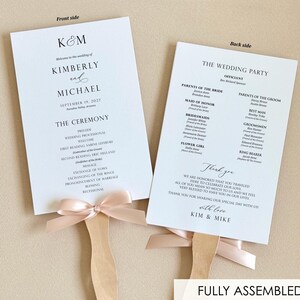 May include: Double-sided wedding program fans with a peach-colored ribbon bow. The front side features the text "K&M Kimberly and Michael September 19, 2027" and the ceremony details. The back side features the wedding party list and the text "Thank you with love Kim & Mike".