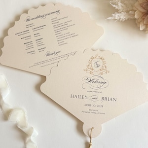 May include: Two fan-shaped wedding programs printed on cream cardstock with scalloped edges. One side displays the ceremony order, while the other features a gold crest, the names Hailey and Brian, the date April 30, 2028, and a gold tassel.