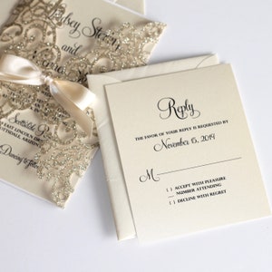 May include: A white RSVP card with black text. The text reads "Reply" in a cursive font. The text also reads "The favor of your reply is requested by November 15, 2019". There is a line for the guest's name and three checkboxes for the guest to indicate their response.