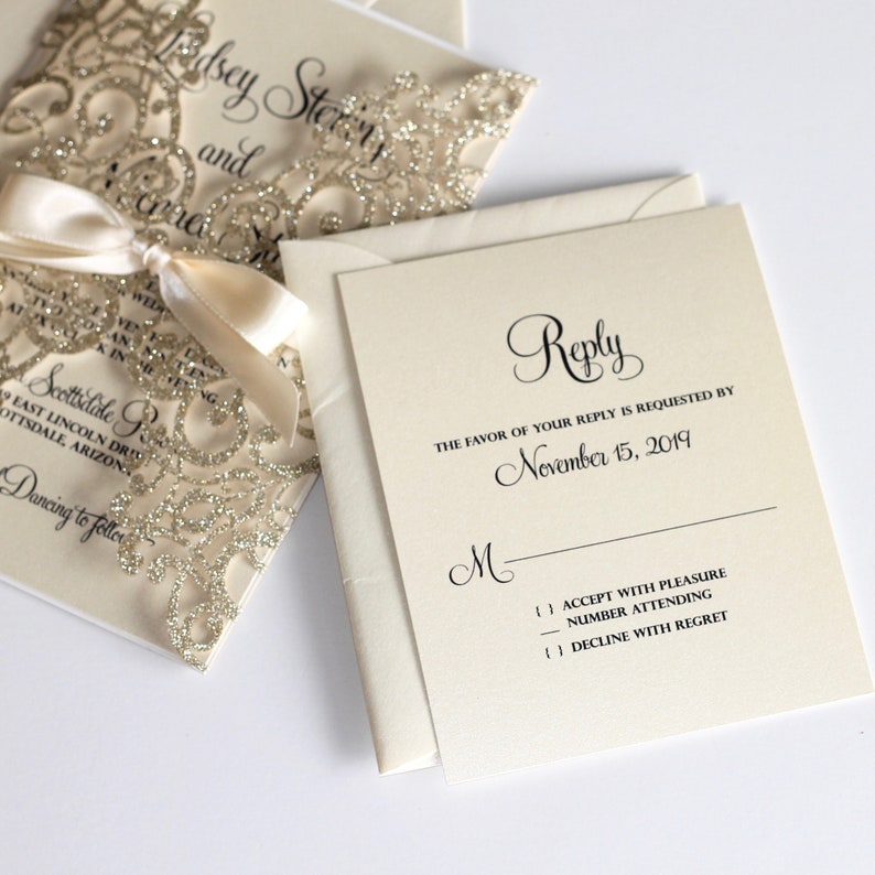 May include: A white RSVP card with black text. The text reads "Reply" in a cursive font. The text also reads "The favor of your reply is requested by November 15, 2019". There is a line for the guest's name and three checkboxes for the guest to indicate their response.