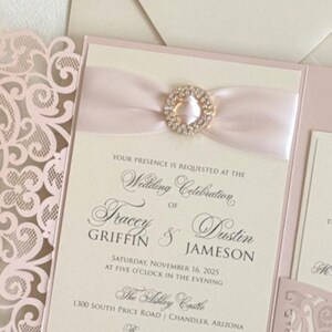 May include: A blush pink and ivory wedding invitation with a laser-cut design. The invitation features a satin ribbon with a rhinestone embellishment. The text on the invitation reads "Your presence is requested at the wedding celebration of Tracey Griffin & Dustin Jameson Saturday, November 16, 2025 at five o'clock in the evening The Ashley Castle 1300 South Price Road | Chandler, Arizona Reception to follow EmbellishedPaperie.Etsy.com"