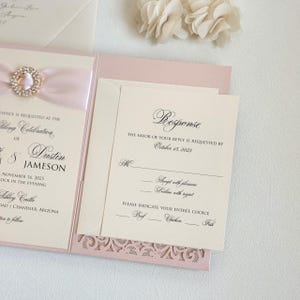 May include: A pink and ivory wedding invitation with a lace design. The invitation includes the names Dustin and Jameson, the date November 16, 2025, and the location Ashley Castle. The RSVP card requests a response by October 15, 2025, and includes options for entree choices: Beef, Chicken, or Fish.
