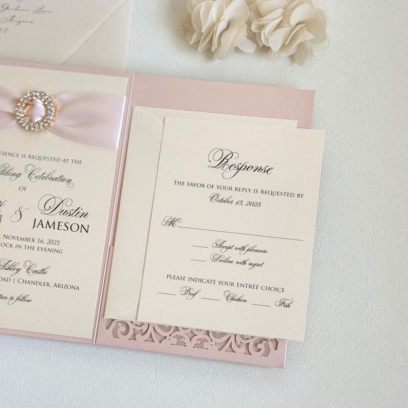 May include: A pink and ivory wedding invitation with a lace design. The invitation includes the names Dustin and Jameson, the date November 16, 2025, and the location Ashley Castle. The RSVP card requests a response by October 15, 2025, and includes options for entree choices: Beef, Chicken, or Fish.