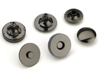 May include: Six black metal snap fasteners, some with a raised center, others with a flat top. These fasteners are used for clothing and other projects.