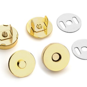 May include: Four gold-toned magnetic closures for sewing projects. Two closures have a raised, round top, and two have a flat top with a small, raised ring. Two silver-toned metal plates with two slots each are also included.