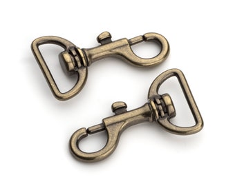 May include: Two antique gold metal swivel clasps with a D-ring. The clasps are closed and ready to be attached to a leash or other item.