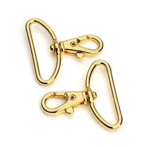 May include: Two gold-toned metal swivel clasps with a D-ring on each. The clasps are designed for attaching to bags, straps, or other accessories.