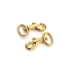 May include: Two gold-toned metal swivel clasps, also known as trigger snaps, are shown on a white background.