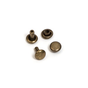 May include: Four antique brass rivets on a white background. The rivets include two with a post and cap, and two with a rounded cap. The rivets are a warm, metallic color, and are likely used for leathercraft or garment construction.