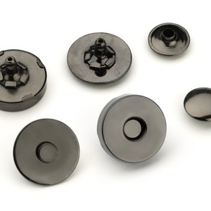 May include: Six black metal snap fasteners, some with a visible metal post, others with a flat surface. These fasteners are commonly used for clothing and crafts.