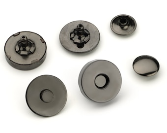May include: Six black metal snap fasteners, some with a visible metal post, others with a flat surface. These fasteners are commonly used for clothing and crafts.